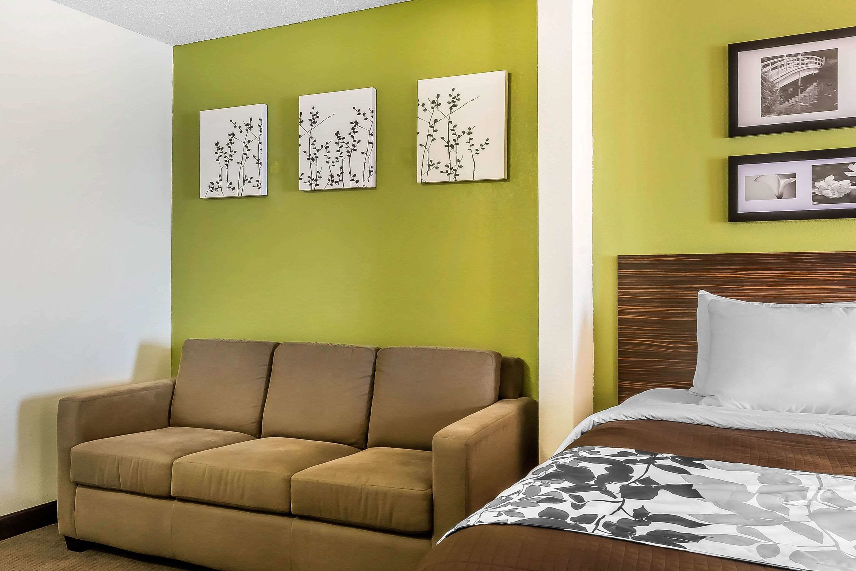 A hotel room with a green wall, a brown sofa, a bed with white bedding, and three framed pictures on the wall.