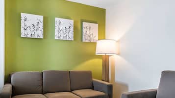 Um quarto com uma parede verde, um sofá marrom, uma luminária e três obras de arte emolduradas.