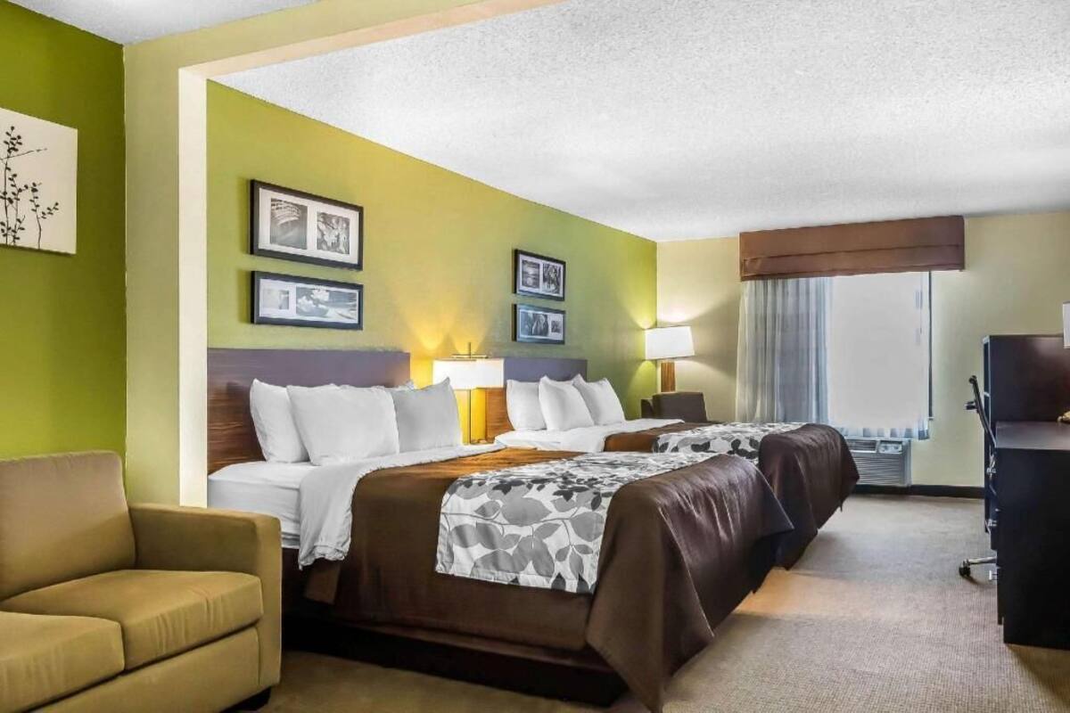 A hotel room with two beds, a sofa, a desk, and framed pictures on the walls.