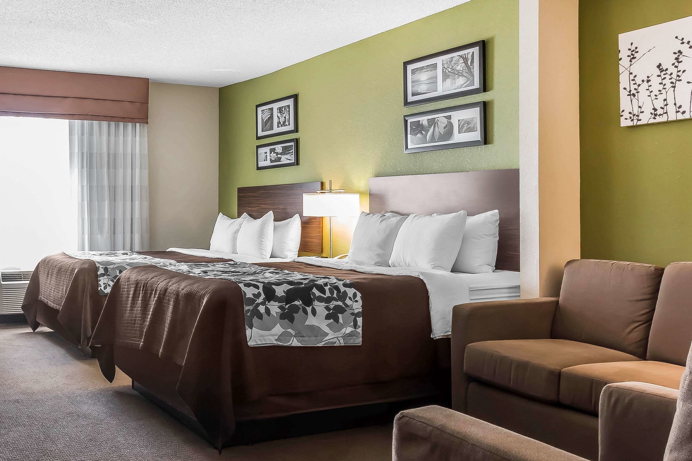 A hotel room with a bed, a sofa, a lamp, and framed pictures on the wall.