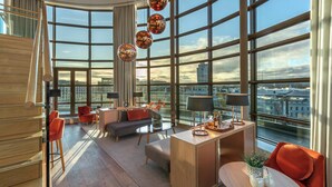 Een moderne woonkamer met grote ramen, een bank, een salontafel en een bureau met een lamp.