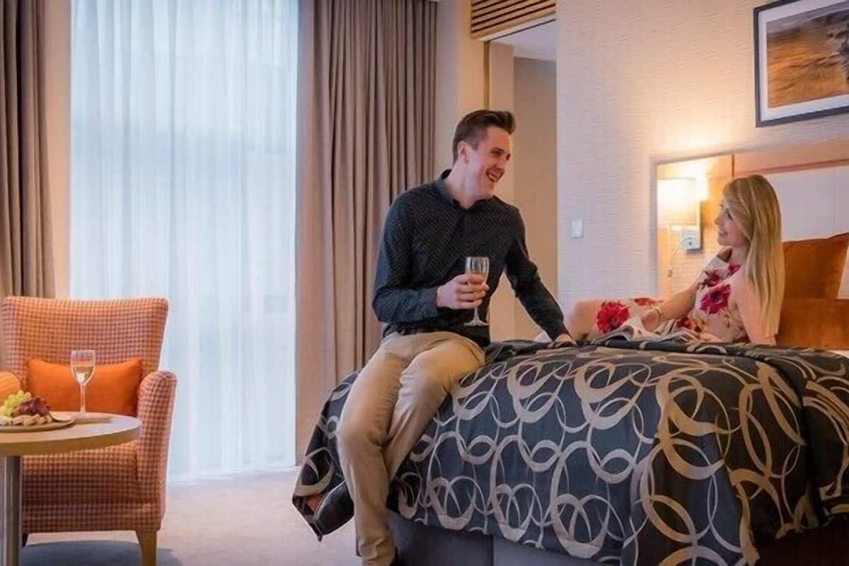 Ein Hotelzimmer mit einem Bett, einem Sessel mit einer Obstplatte und einem Weinglas, sowie einem Gemälde an der Wand.
