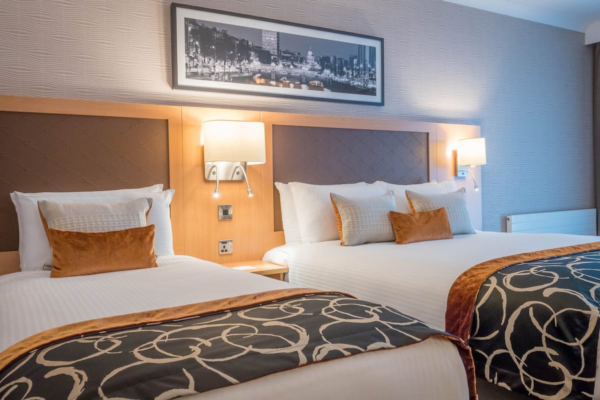 Ein Hotelzimmer mit zwei Betten, jeweils mit Kopfteil, einem Wandbild und Nachttischlampen.