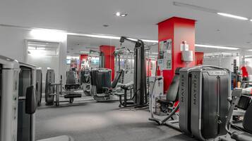 A gym with various exercise machines, red walls, and a clean, modern design.