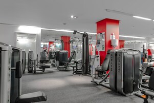 Ein Fitnessstudio mit verschiedenen Trainingsgeräten, roten Wänden und einem klaren, modernen Design.