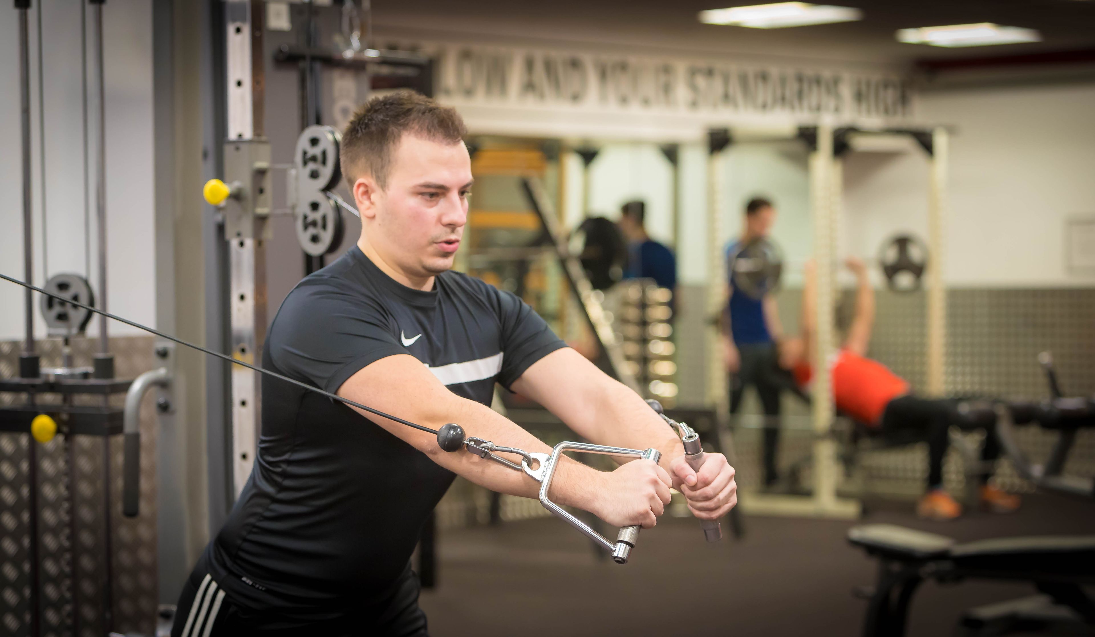 A man using a cable machine in a gym with visible weight plates and a mirror.