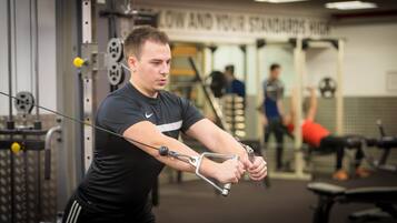 A man using a cable machine in a gym with visible weight plates and a mirror.