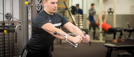 A man using a cable machine in a gym with visible weight plates and a mirror.