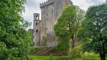 A historic stone castle with a prominent tower, surrounded by lush greenery and a well-maintained lawn.