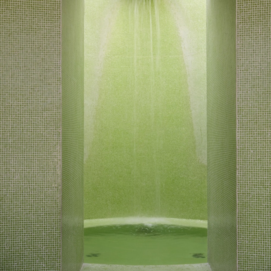 A bathroom with a green-tiled wall and a shower area.