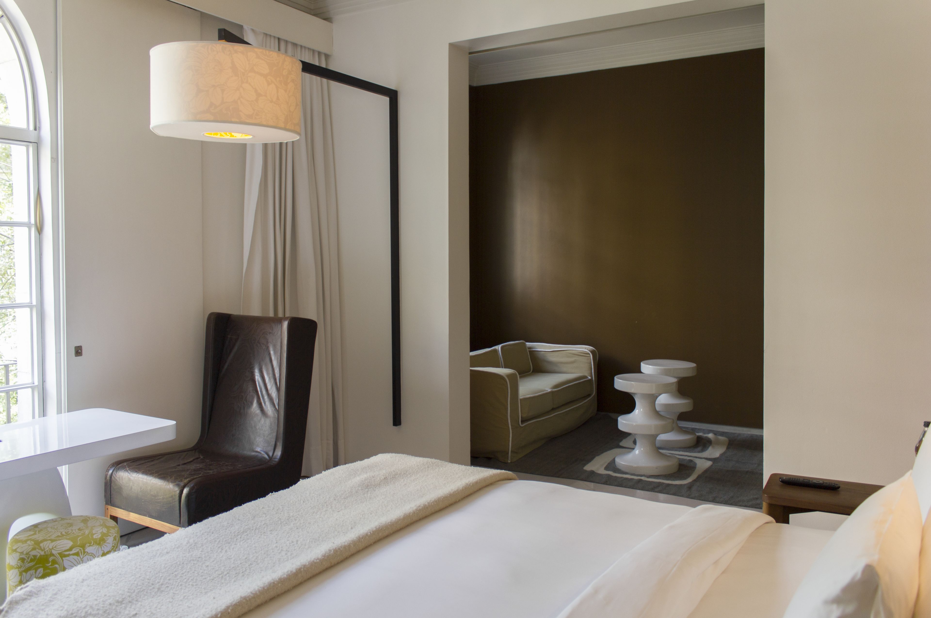 A hotel room with a bed, a desk, a chair, a sofa, and a lamp.