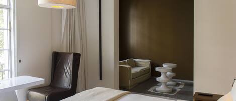 A hotel room with a bed, a desk, a chair, a sofa, and a lamp.