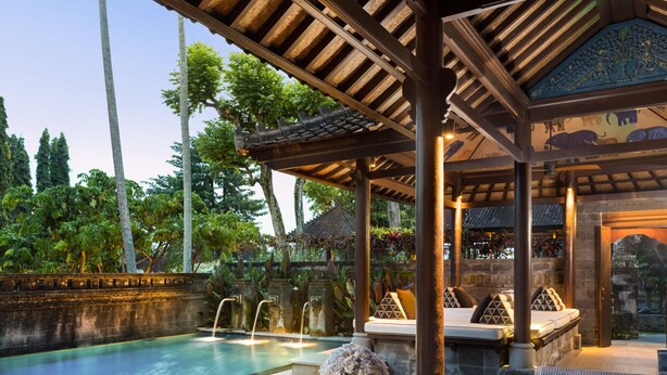 A poolside area with a wooden deck, lounge chairs, and a small table with a vase. - Tanah Gajah, a Resort by Hadiprana (Ubud)