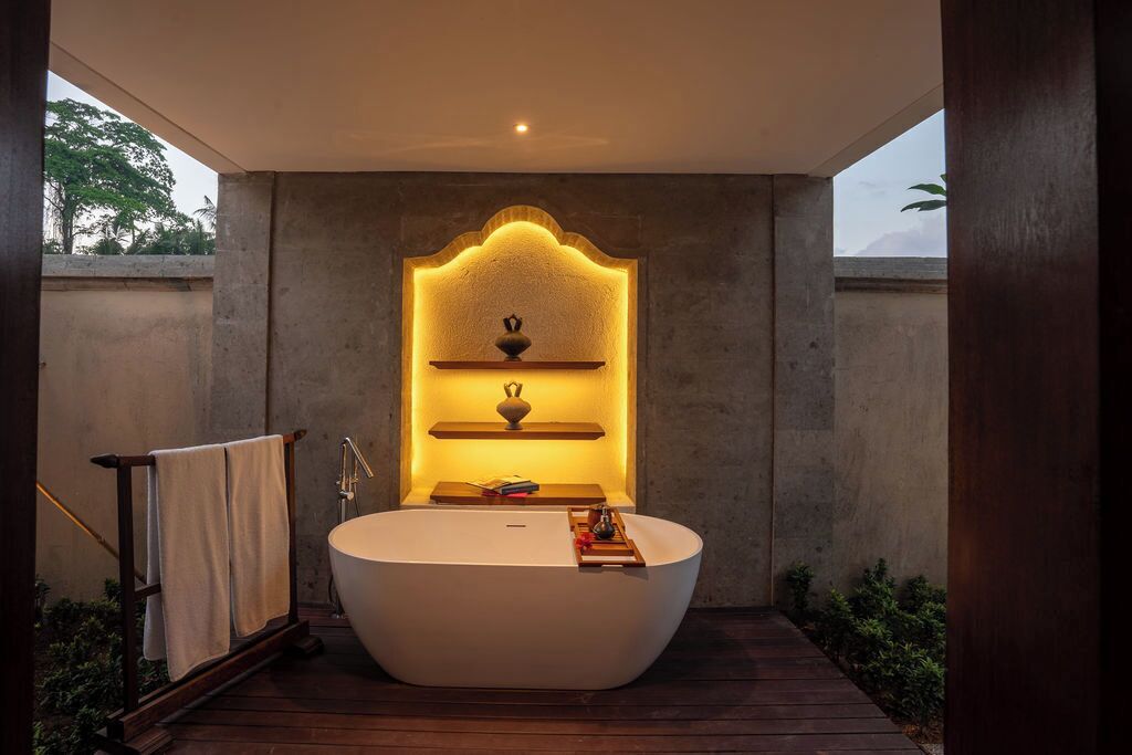 A modern bathroom with a freestanding bathtub, a built-in shelf with decorative items, and a towel rack.