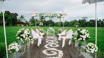 Una terraza de madera con sillas blancas y un camino decorado con flores.
