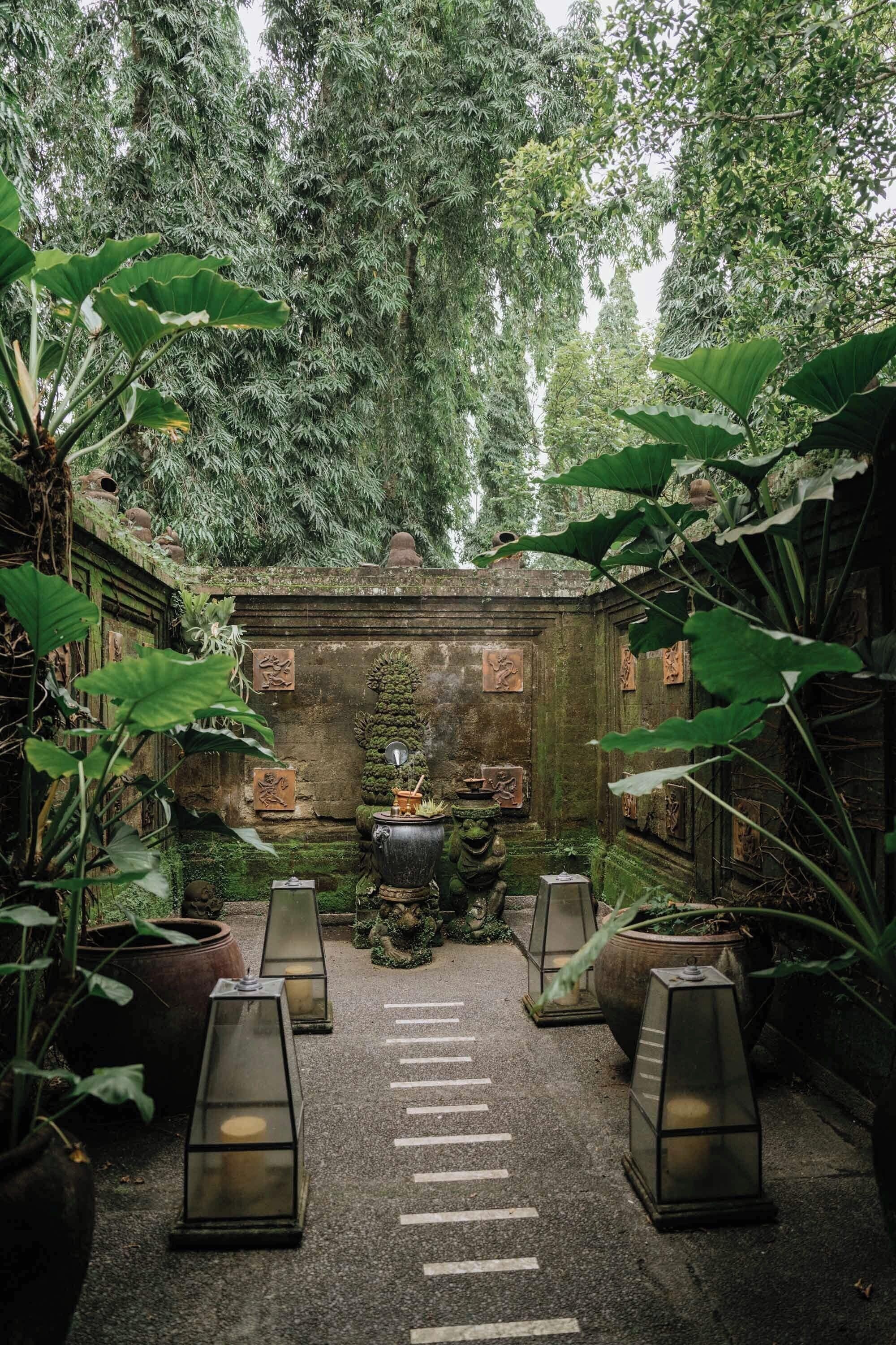 Un patio con una estructura de piedra central, rodeado de plantas en macetas y faroles.