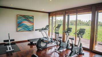 A gym with exercise equipment and a large window offering a view of a green landscape.