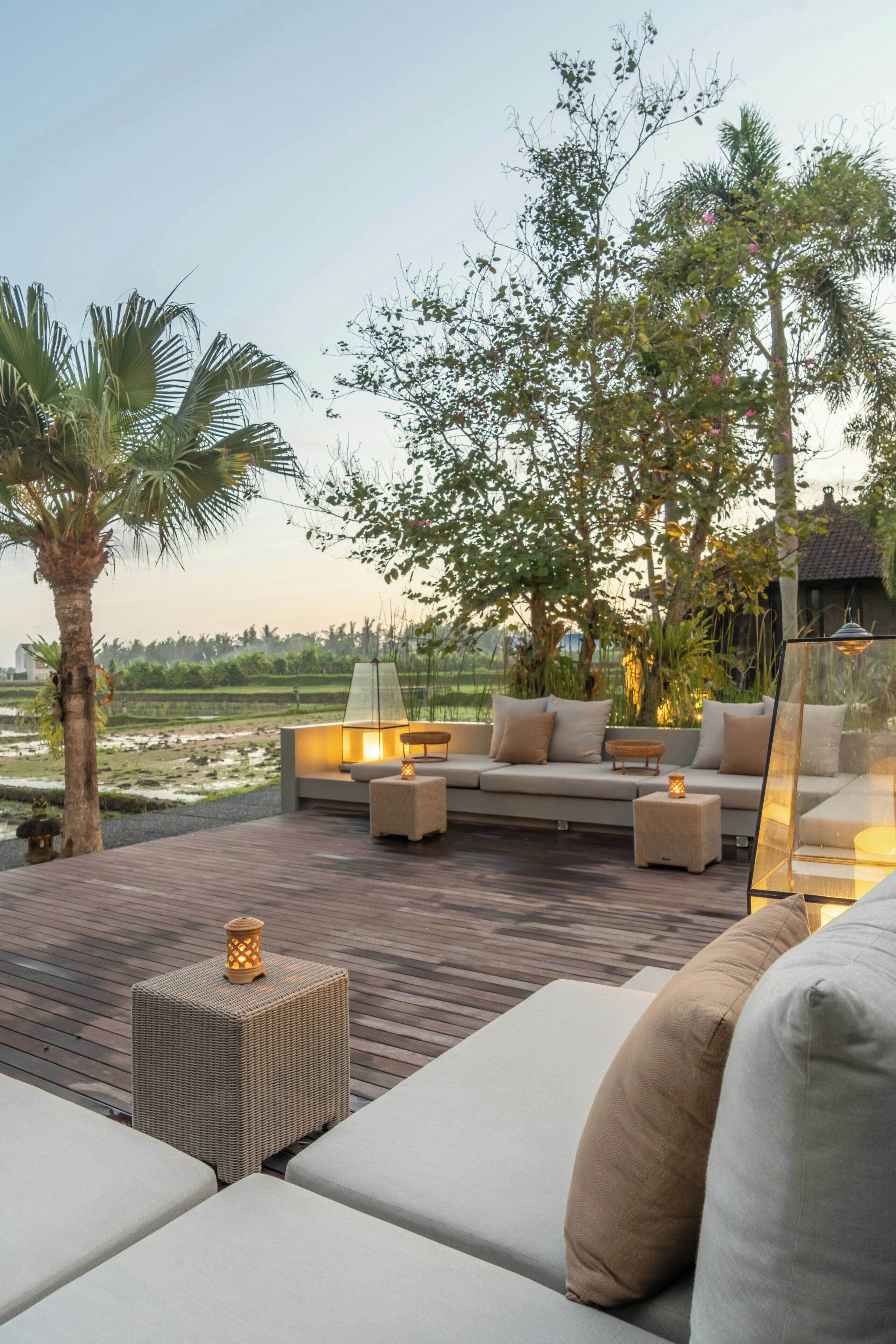 An outdoor seating area with a sofa, cushions, and a small table, surrounded by trees and a view of a landscape.