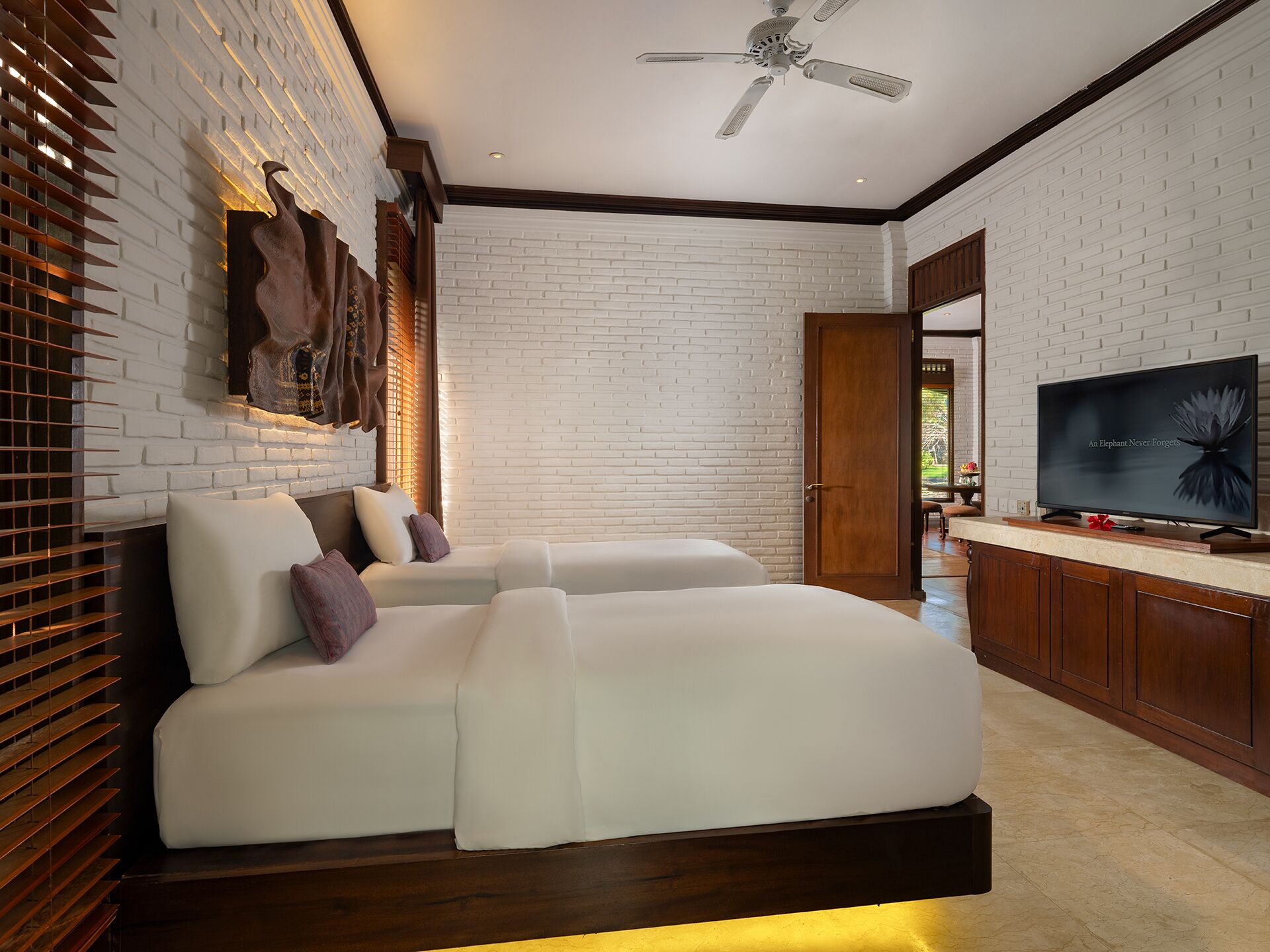 A modern bedroom with a white brick wall, a ceiling fan, a flat-screen TV, and a large bed with white bedding.
