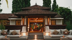A traditional building with a tiled roof, a central entrance with steps, and a seating area with cushions and tables. - Tanah Gajah, a Resort by Hadiprana (Ubud)