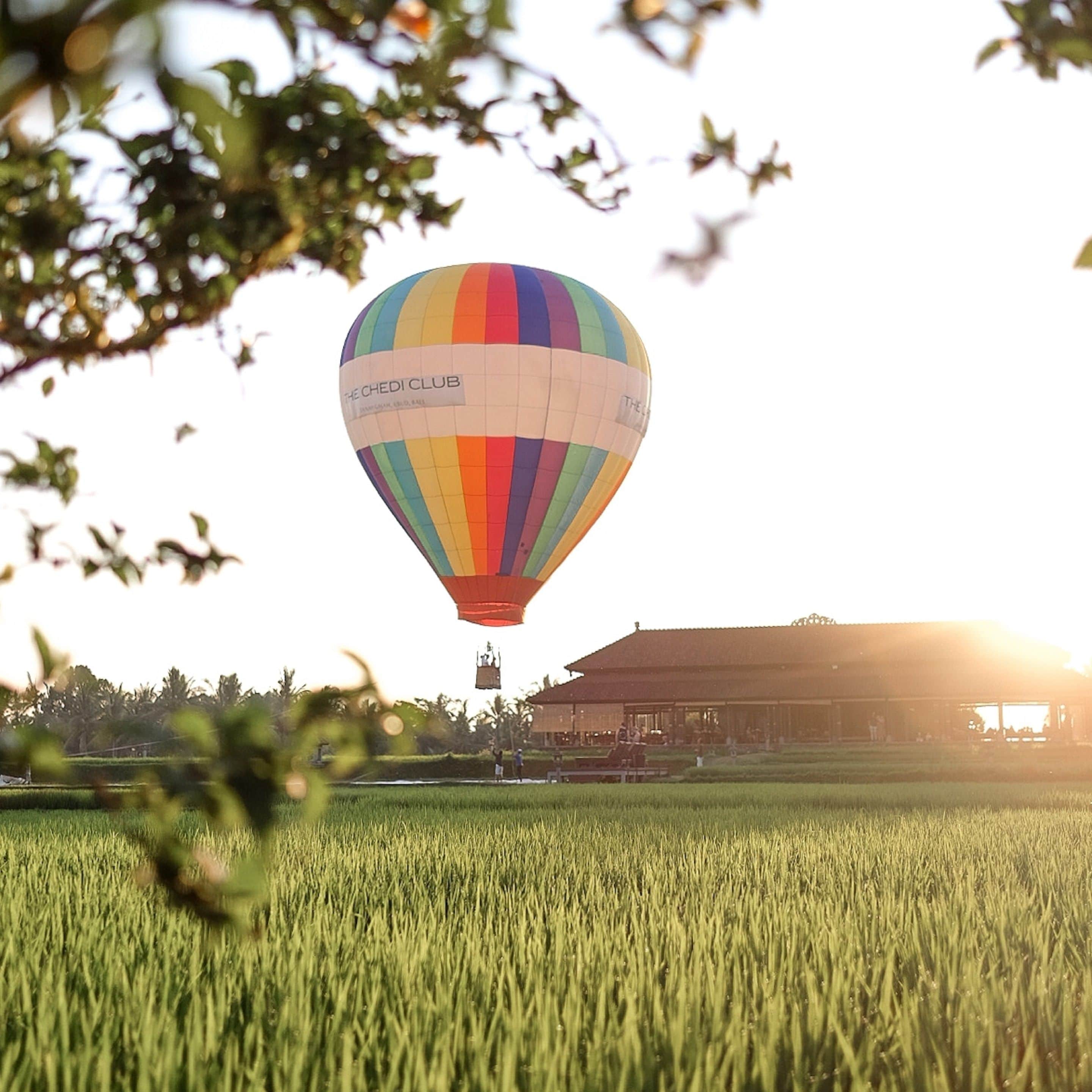 Un globo aerostático con la inscripción "The Chedi Club" volando sobre un campo con un edificio al fondo.