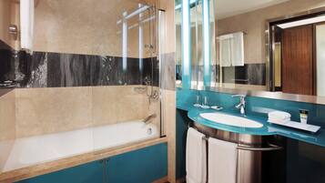 A modern bathroom with a glass-enclosed shower, a white bathtub, and a blue vanity with a glass sink.