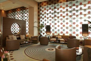 A modern lobby with a circular mirror, sofas, armchairs, and a patterned carpet.