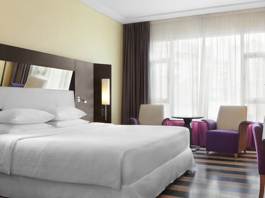 Habitación de hotel con una cama grande, un escritorio, dos sillas y una ventana con cortinas.