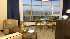 A hotel room with a dining area, a large window with a city view, and a fruit bowl on the table. - Four Points by Sheraton Le Verdun (Beirut)