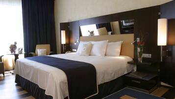 A hotel room with a large bed, bedside tables, a nightstand, a desk, and a chair.