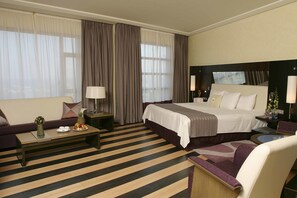 A hotel room with a large bed, a sofa, a coffee table with fruit, a desk, and a chair. - Four Points by Sheraton Le Verdun (Beirut)