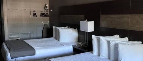 Habitación de hotel con dos camas, ventilador de techo, mesita de noche con lámpara y televisor montado en la pared.