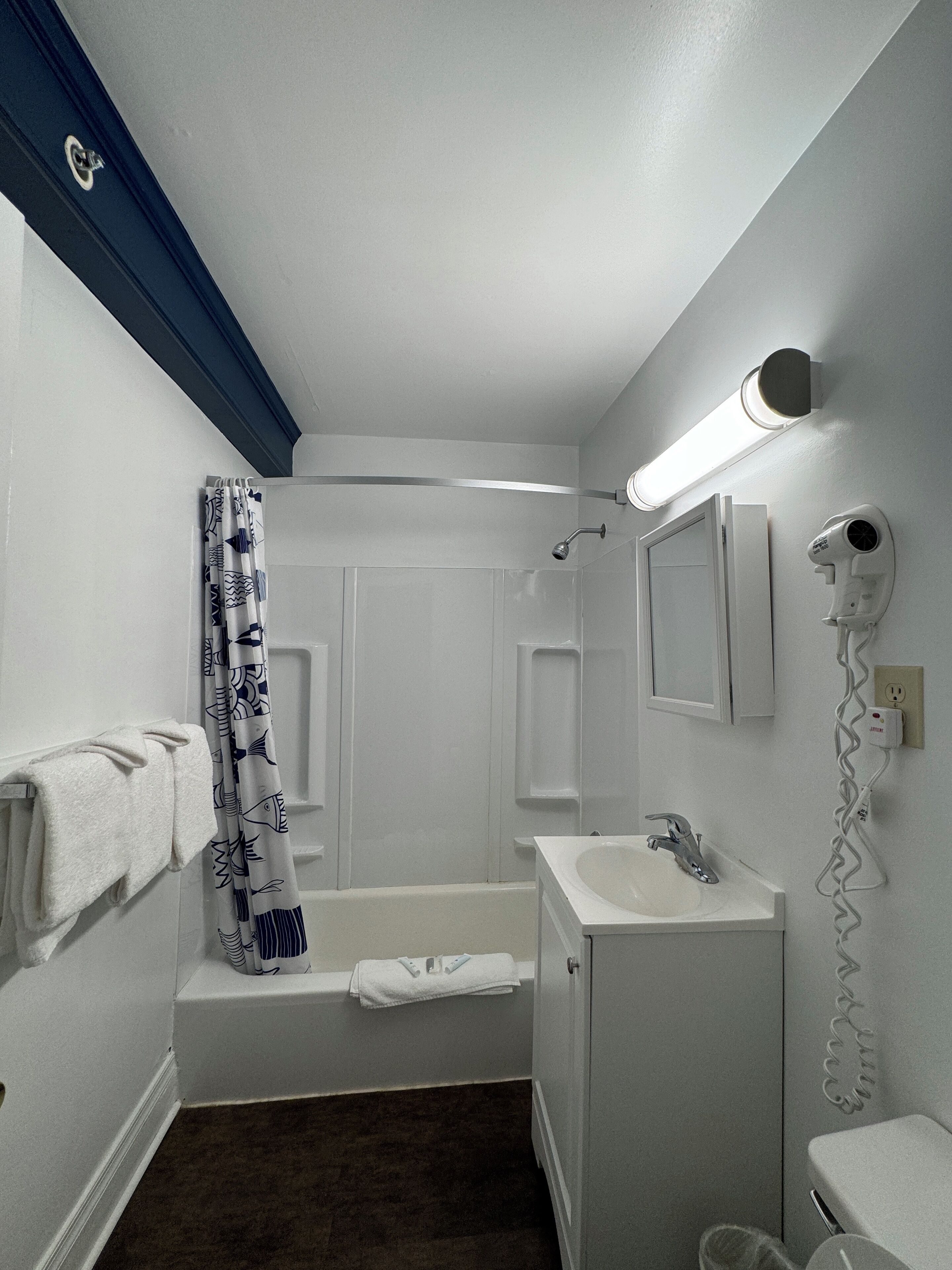 Un bagno con una vasca, un lavandino, un portasciugamani e un asciugacapelli a parete.