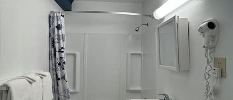 Un baño con bañera, lavamanos, toallero y secador de pelo en la pared.