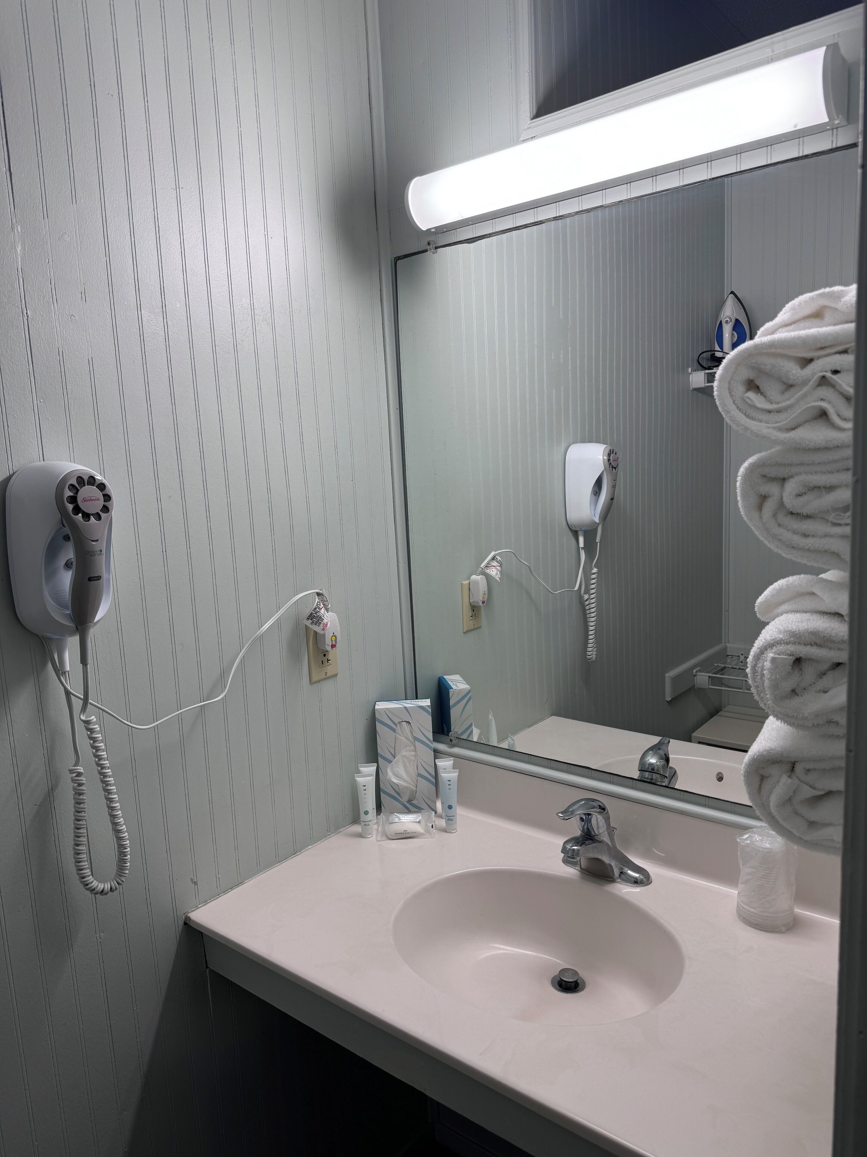 A bathroom with a white sink, a mirror, a hairdryer, and a towel rack.