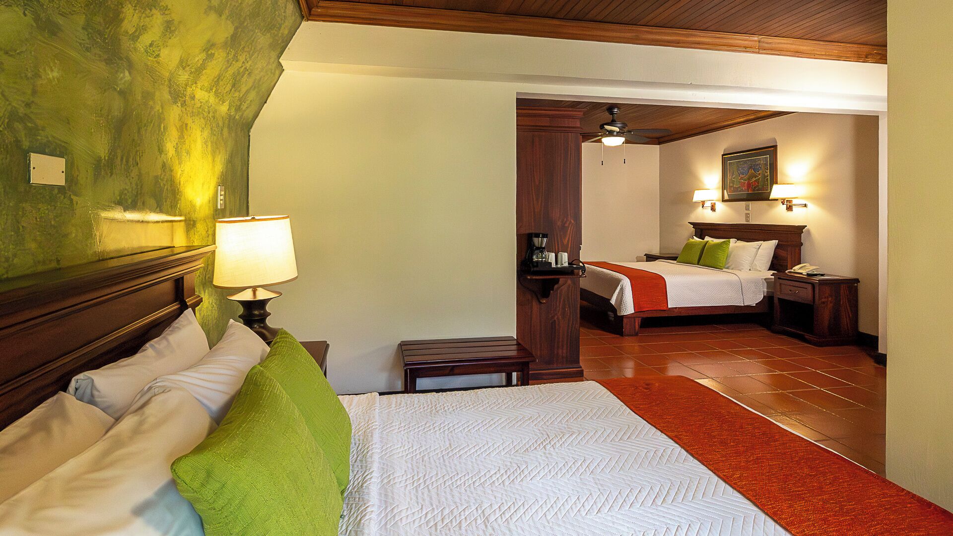 A hotel room with a bed, a nightstand, a lamp, a coffee maker, and a bedside table.