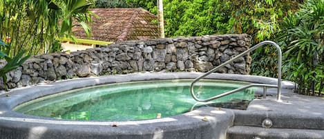 A hot tub surrounded by a stone wall and lush greenery.