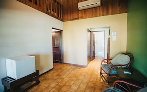 Relax in this spacious room with a high ceiling, featuring a comfortable bed, a wooden chair, and a small table.