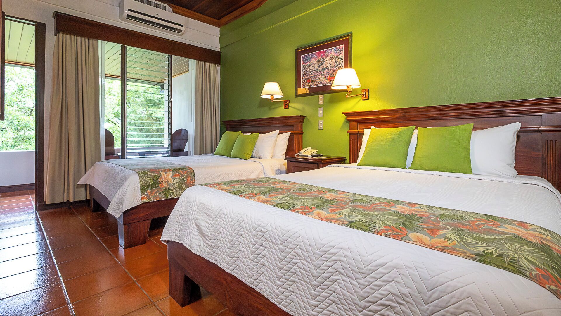 A hotel room with two beds, a large window with curtains, a wall-mounted air conditioner, and a painting above the beds.