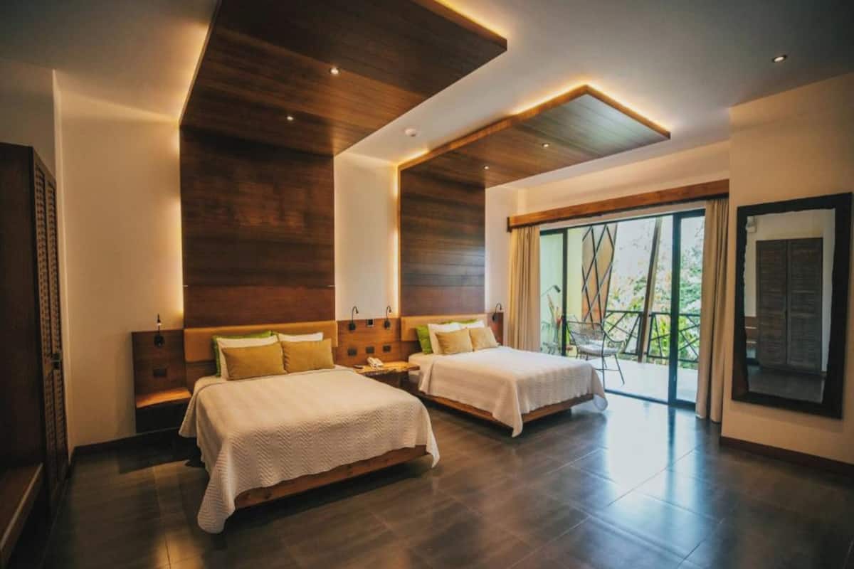 A modern hotel room with two beds, wooden ceiling, large windows, and a balcony.
