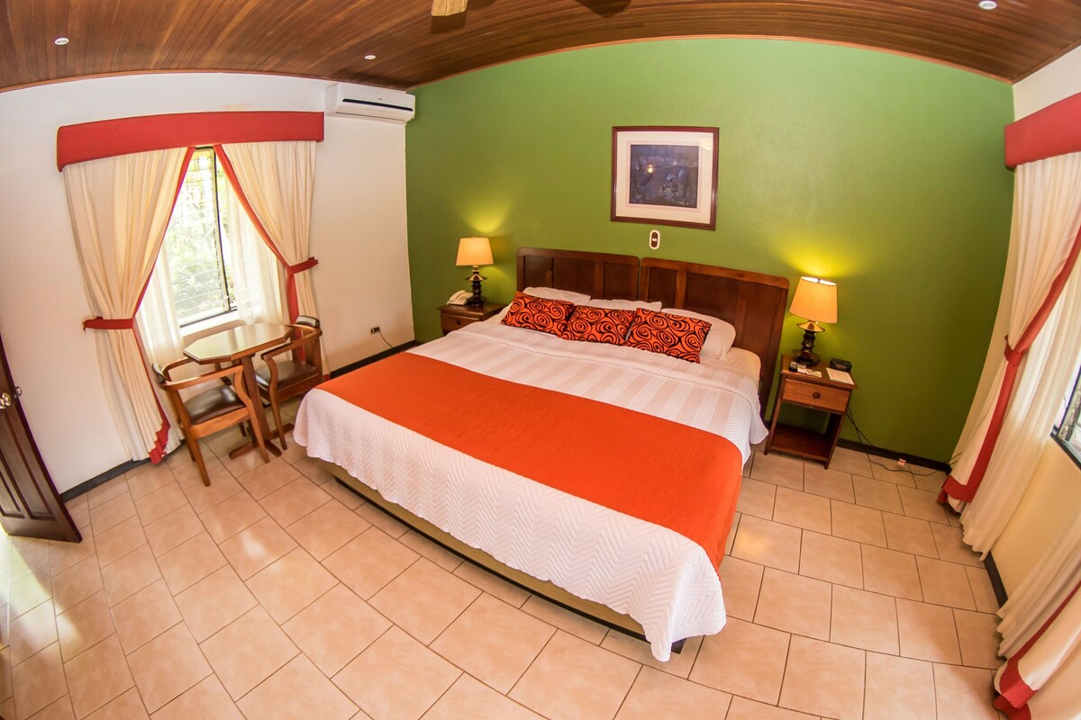 A hotel room with a bed, two bedside tables, a chair, a window with curtains, and a wall-mounted picture.