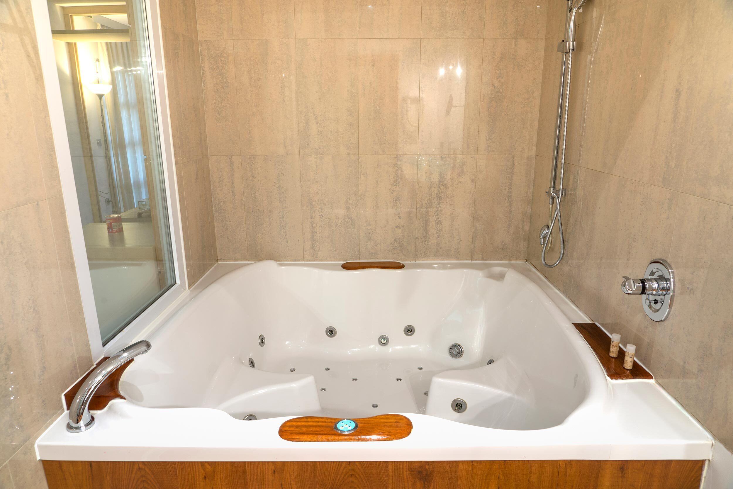 Una bañera blanca grande y separada, con una bandeja de madera y un cabezal de ducha manual.