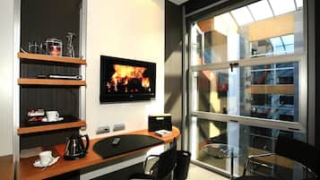 Habitación de hotel moderna con un escritorio de madera, televisor de pantalla plana, cafetera y una mesa de vidrio con sillas.