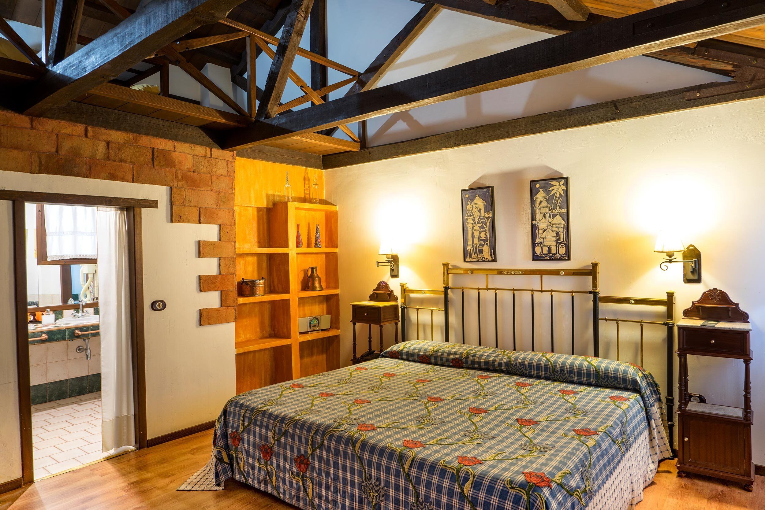 A bedroom with a wooden bed, a shelf with bottles, and a wall-mounted lamp.