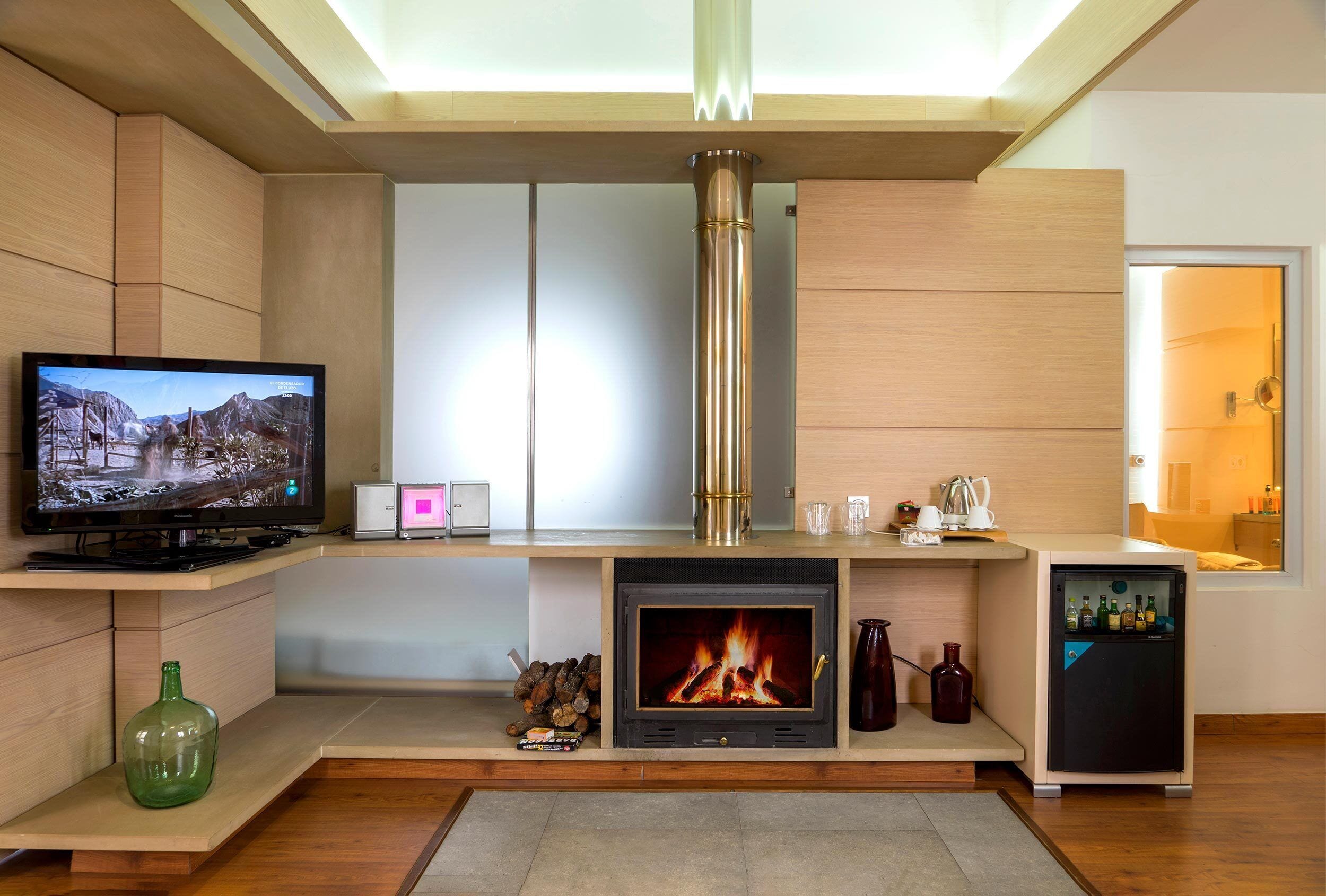 Una sala de estar moderna con chimenea, televisión y un refrigerador pequeño.
