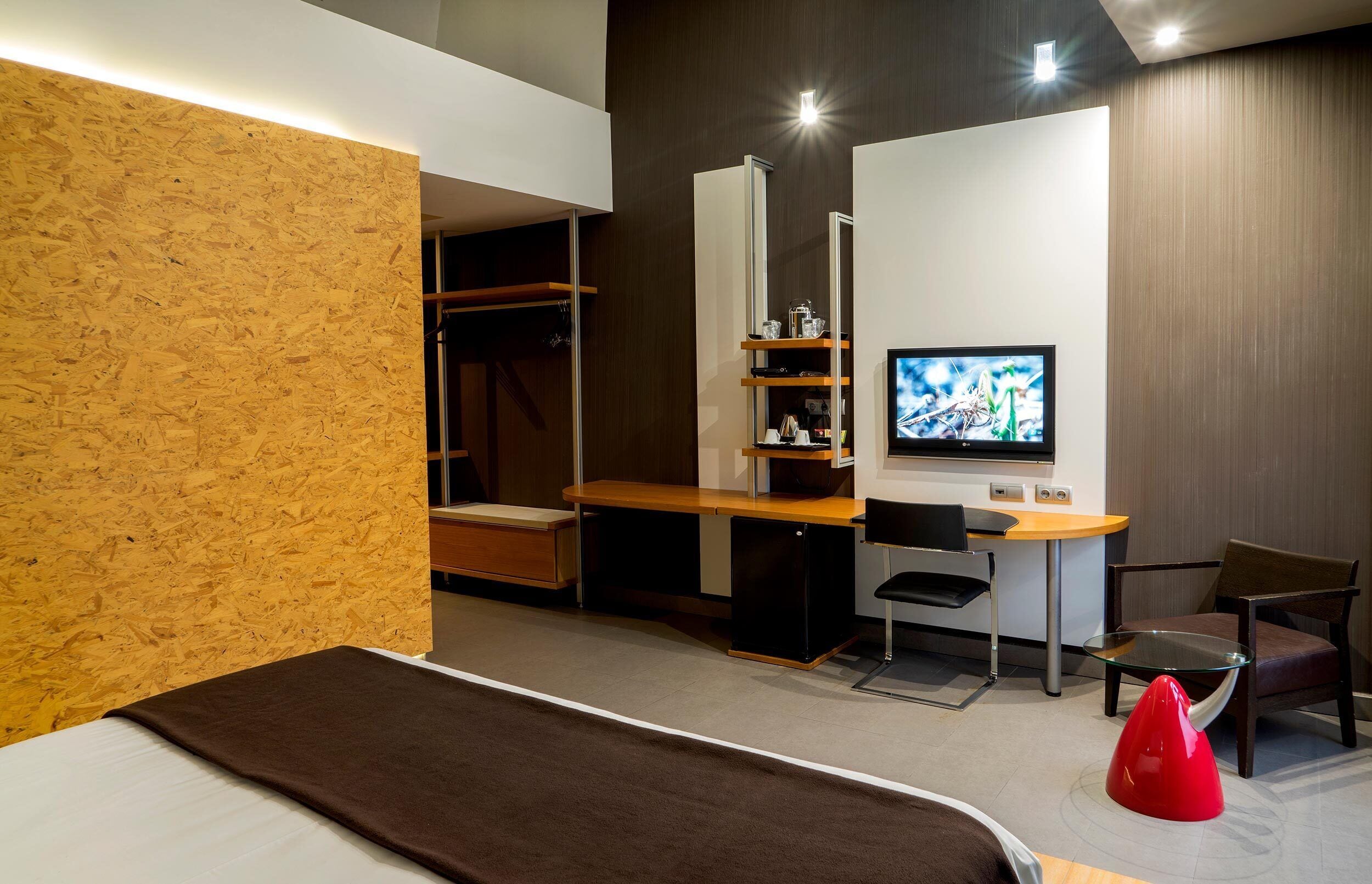 A modern hotel room with a bed, a desk with a computer, a TV, and a wardrobe.