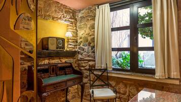 A room with a stone wall, a wooden desk with a green felt surface, a chair, and a window with curtains.