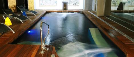 A hot tub with a wooden deck, a metal ladder, and a view of the outdoors through large windows.