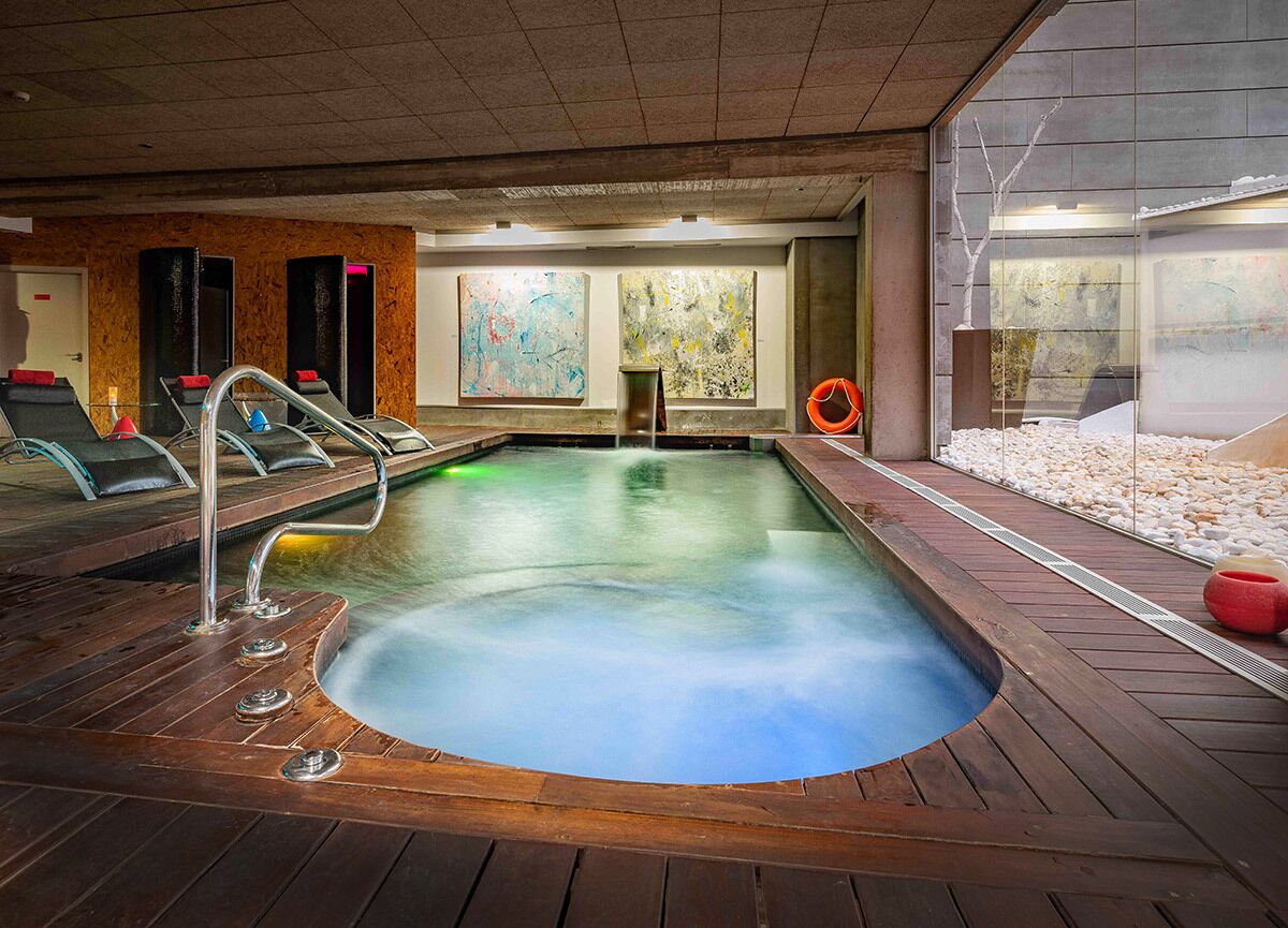 A hot tub area with wooden flooring, a pool, and a view of the city through large windows.
