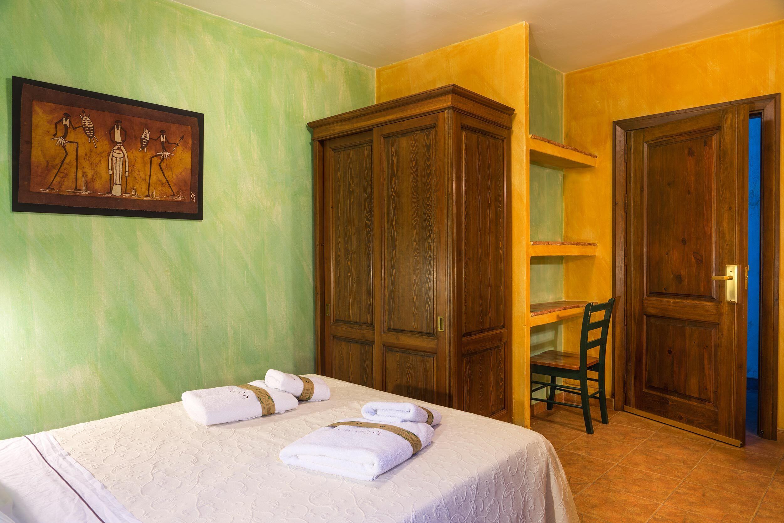 Habitació d'hotel amb un llit, un armari de fusta, una taula de treball amb una cadira i un quadre a la paret.